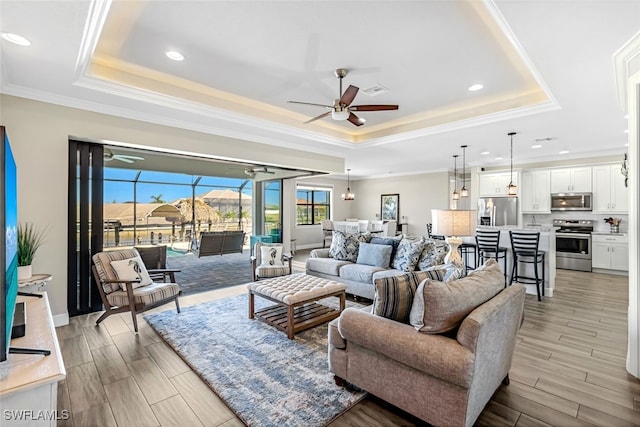 living room with a tray ceiling, ceiling fan, and ornamental molding