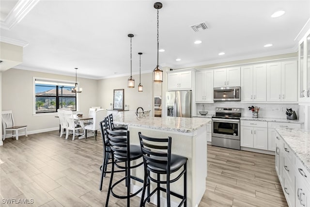 kitchen with pendant lighting, a kitchen island with sink, a kitchen breakfast bar, appliances with stainless steel finishes, and white cabinetry