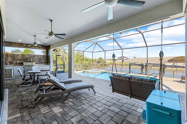 view of patio with glass enclosure, a water view, an in ground hot tub, a grill, and exterior kitchen