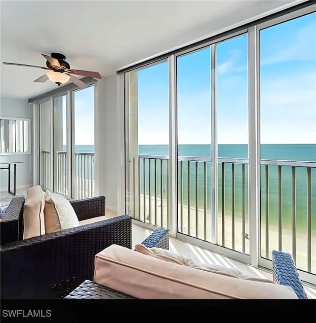 sunroom with ceiling fan, a water view, a beach view, and a wealth of natural light