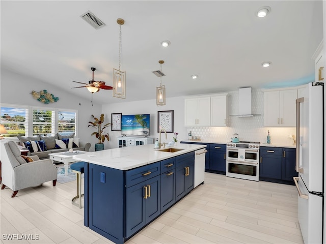 kitchen featuring wall chimney exhaust hood, white appliances, white cabinetry, and blue cabinetry