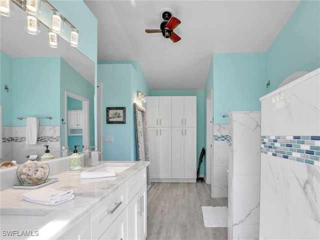 bathroom with ceiling fan, hardwood / wood-style floors, vanity, and tile walls