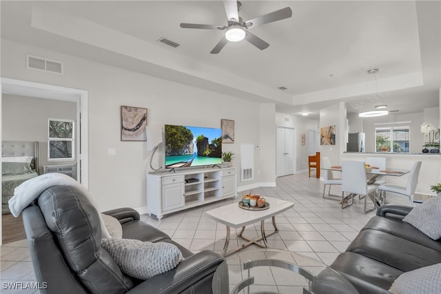 tiled living room with ceiling fan and a raised ceiling