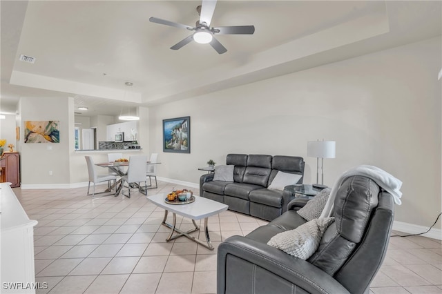 living room featuring a raised ceiling, ceiling fan, and light tile patterned floors