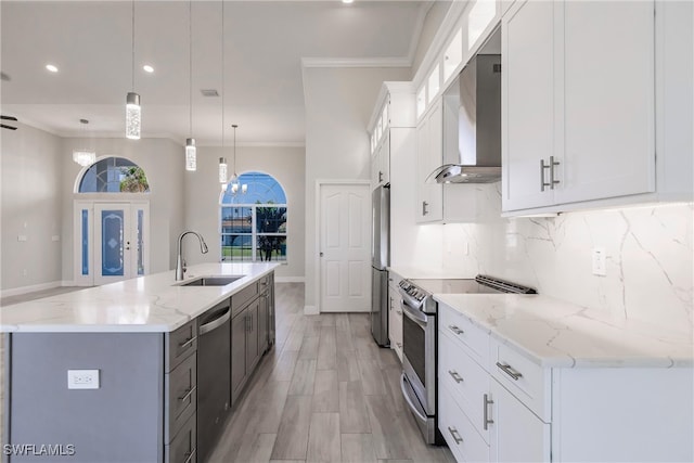 kitchen with white cabinets, sink, wall chimney exhaust hood, appliances with stainless steel finishes, and decorative light fixtures