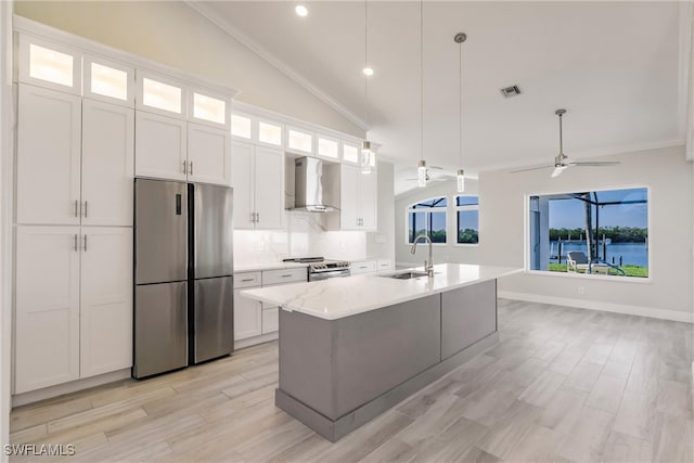 kitchen featuring white cabinets, a center island with sink, vaulted ceiling, wall chimney exhaust hood, and stainless steel appliances