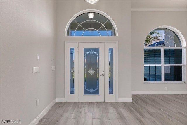 entrance foyer with light hardwood / wood-style flooring, a towering ceiling, a chandelier, and ornamental molding