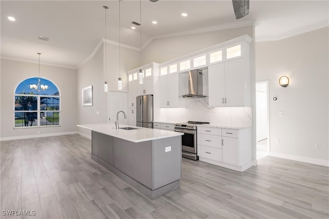 kitchen featuring hanging light fixtures, wall chimney range hood, a center island with sink, white cabinets, and appliances with stainless steel finishes