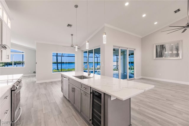 kitchen featuring appliances with stainless steel finishes, a kitchen island with sink, sink, a water view, and wine cooler