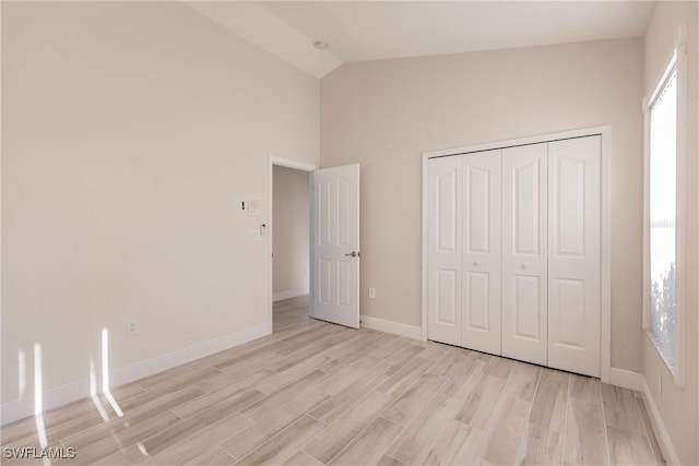 unfurnished bedroom featuring light hardwood / wood-style floors, a closet, and lofted ceiling