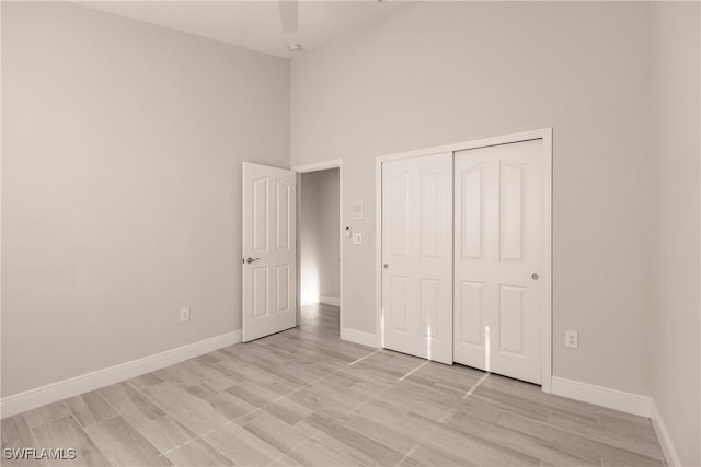 unfurnished bedroom with light wood-type flooring, a towering ceiling, a closet, and ceiling fan