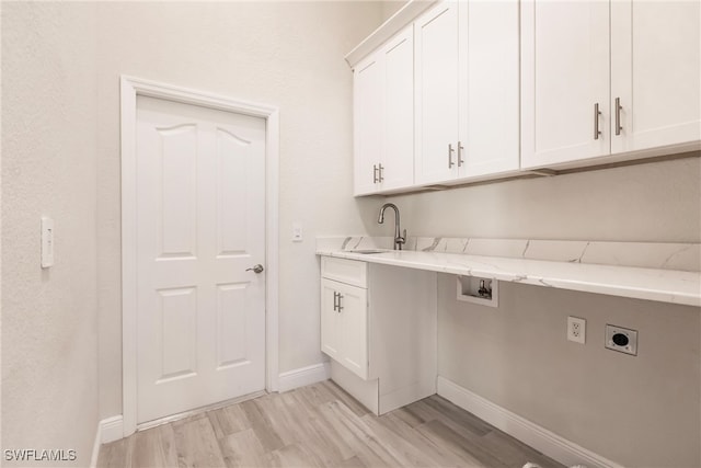 clothes washing area with electric dryer hookup, sink, cabinets, and light wood-type flooring