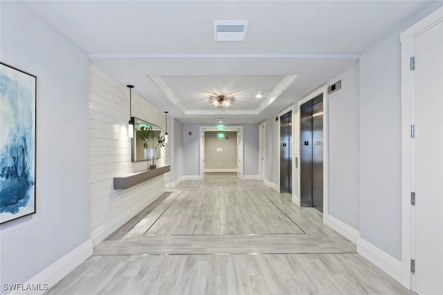 hall featuring elevator, a tray ceiling, and light hardwood / wood-style flooring