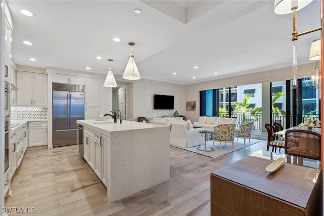 kitchen featuring pendant lighting, stainless steel appliances, a center island with sink, and white cabinets