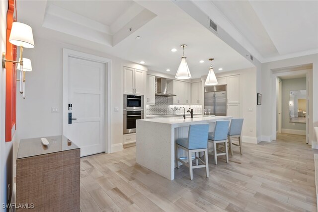 kitchen with pendant lighting, an island with sink, white cabinets, stainless steel appliances, and wall chimney exhaust hood