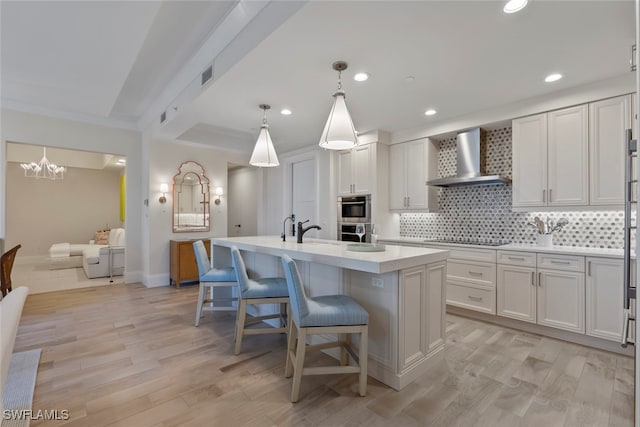 kitchen with wall chimney exhaust hood, a breakfast bar, white cabinetry, a center island with sink, and pendant lighting