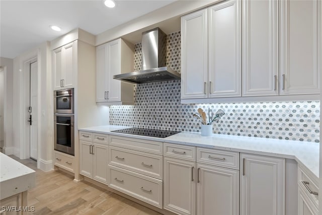 kitchen with black electric cooktop, white cabinets, stainless steel double oven, and wall chimney range hood