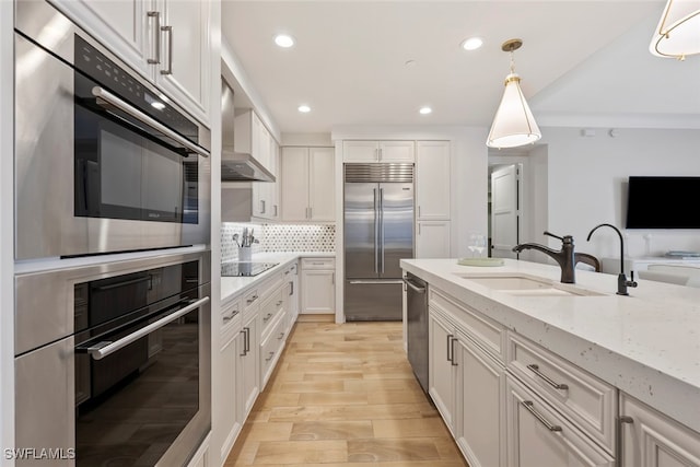 kitchen with sink, decorative light fixtures, white cabinets, stainless steel appliances, and wall chimney range hood