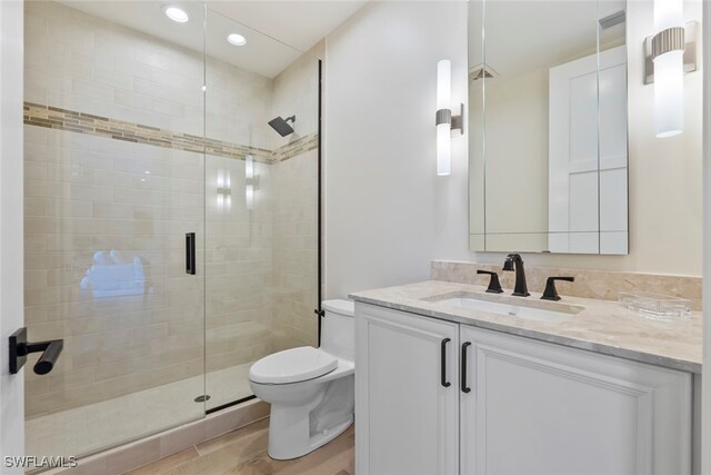 bathroom featuring vanity, wood-type flooring, a shower with shower door, and toilet