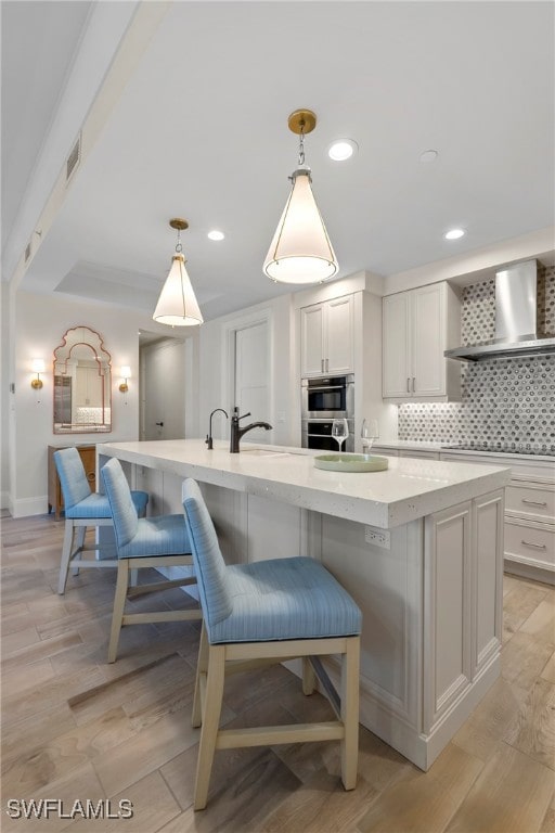 kitchen with a breakfast bar, pendant lighting, tasteful backsplash, an island with sink, and wall chimney exhaust hood