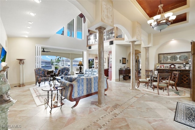 living room featuring a high ceiling, ceiling fan with notable chandelier, decorative columns, and crown molding