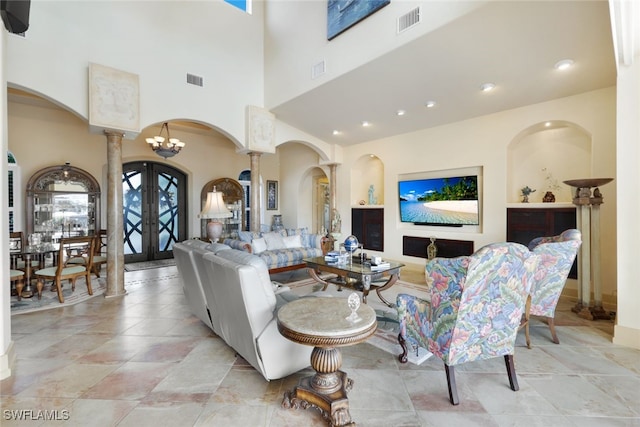 living room with a chandelier, french doors, a towering ceiling, and ornate columns