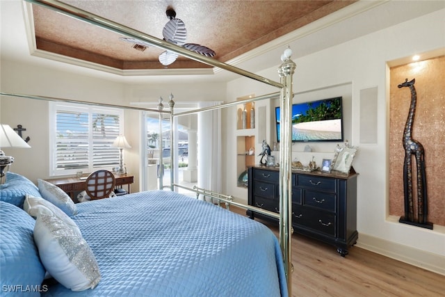 bedroom with a textured ceiling, light hardwood / wood-style floors, a raised ceiling, and ornamental molding