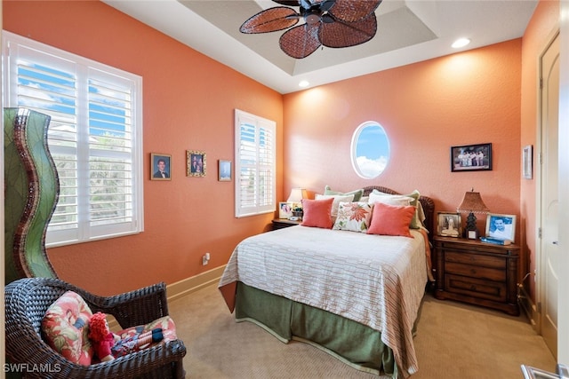 bedroom featuring ceiling fan, light colored carpet, and a tray ceiling