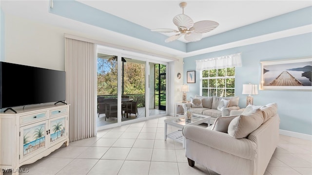 tiled living room with ceiling fan and a tray ceiling