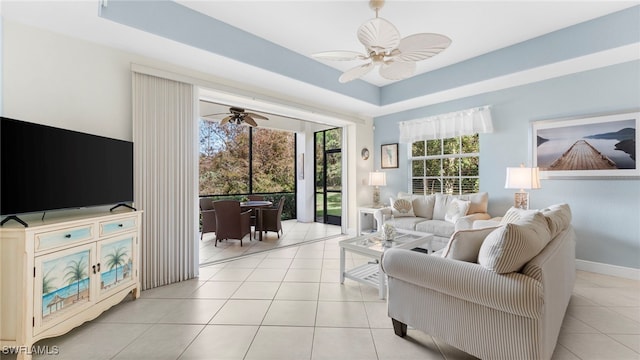 living room featuring a raised ceiling, light tile patterned floors, and ceiling fan