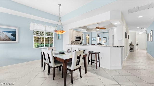 dining room with light tile patterned floors, a tray ceiling, and ceiling fan