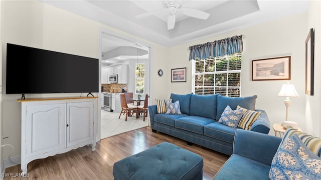 living room featuring ceiling fan, a tray ceiling, and light wood-type flooring