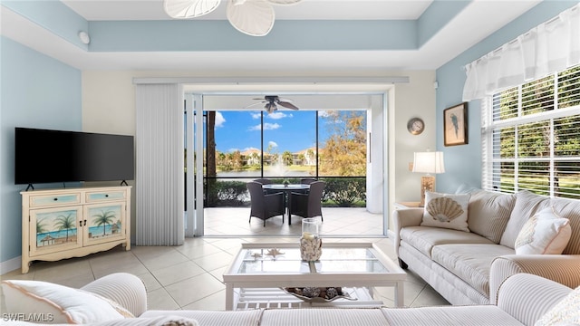 tiled living room with plenty of natural light, a raised ceiling, and ceiling fan