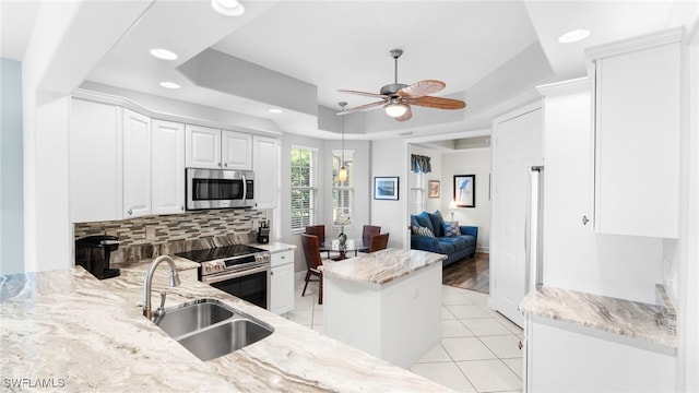 kitchen featuring sink, white cabinetry, appliances with stainless steel finishes, a tray ceiling, and light stone countertops