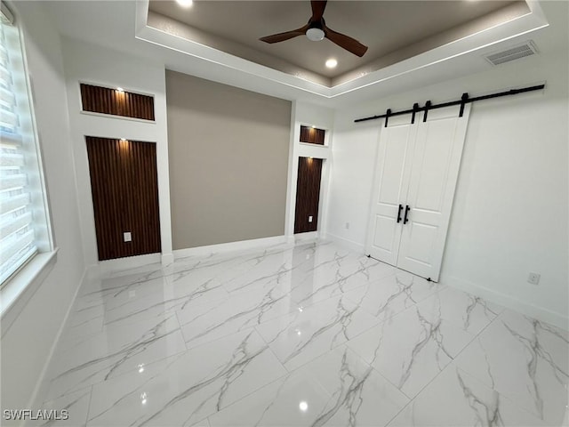 unfurnished bedroom featuring a closet, a tray ceiling, a barn door, and ceiling fan