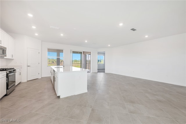 kitchen featuring a kitchen island with sink, sink, light tile patterned floors, white cabinetry, and stainless steel appliances