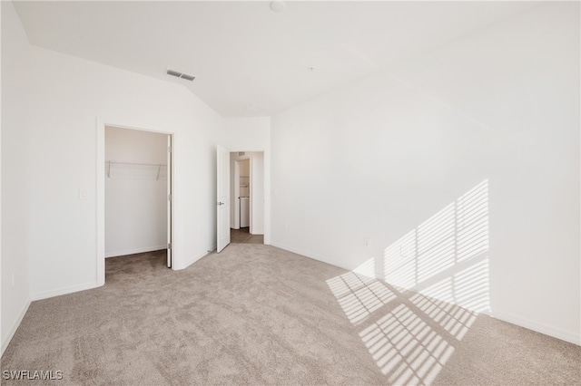 unfurnished bedroom featuring vaulted ceiling, light colored carpet, a walk in closet, and a closet