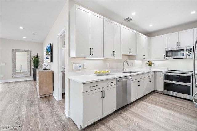 kitchen with white cabinets, sink, stainless steel appliances, and light hardwood / wood-style flooring