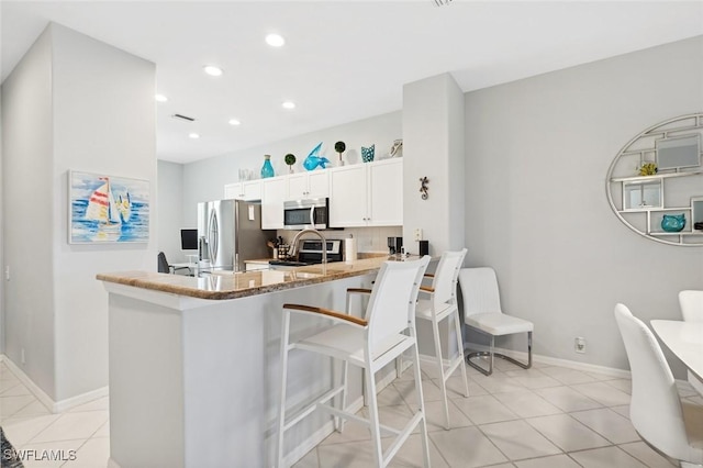 kitchen with kitchen peninsula, light stone countertops, stainless steel appliances, white cabinets, and light tile patterned flooring