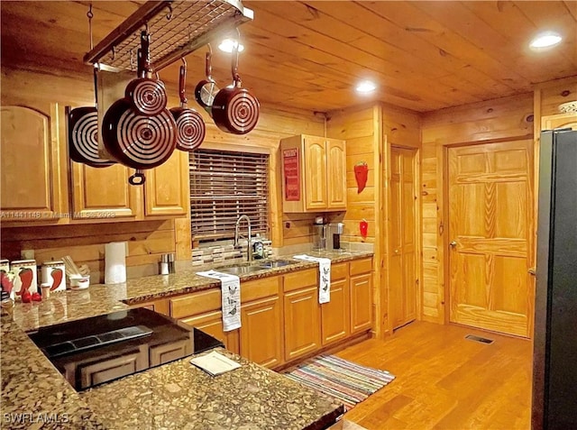 kitchen featuring sink, light stone counters, wood walls, refrigerator, and light wood-type flooring