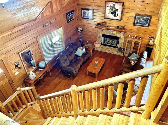 living room featuring high vaulted ceiling, hardwood / wood-style flooring, a stone fireplace, and wooden walls