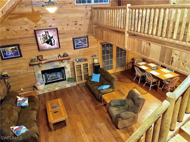 living room with a stone fireplace, wood-type flooring, and wooden walls