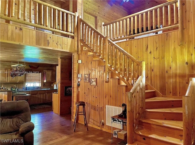 staircase with wood-type flooring, wooden walls, and a towering ceiling