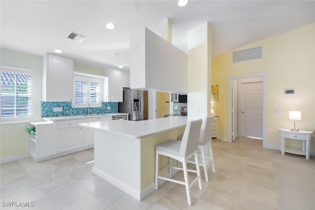 kitchen featuring appliances with stainless steel finishes, tasteful backsplash, white cabinetry, a breakfast bar area, and light tile patterned flooring