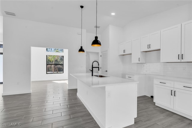 kitchen with white cabinets, decorative light fixtures, a center island with sink, and sink