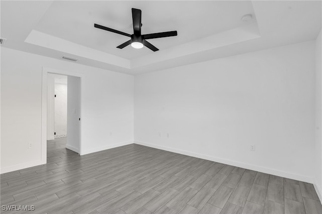 empty room with ceiling fan, a raised ceiling, and light hardwood / wood-style flooring