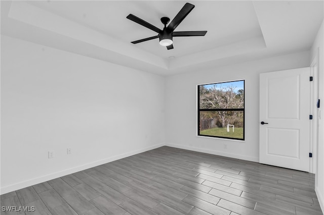 unfurnished room with ceiling fan, light wood-type flooring, and a tray ceiling