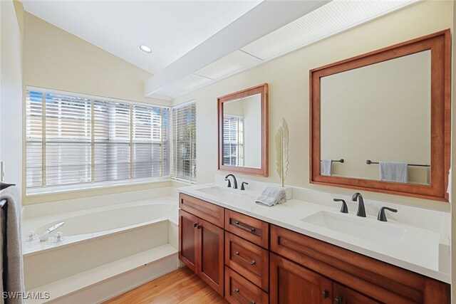 bathroom featuring hardwood / wood-style floors, vanity, vaulted ceiling, and a tub