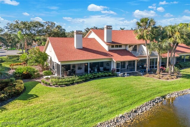 rear view of house featuring a balcony, a water view, and a lawn