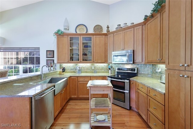 kitchen featuring sink, stainless steel appliances, light stone counters, kitchen peninsula, and light wood-type flooring